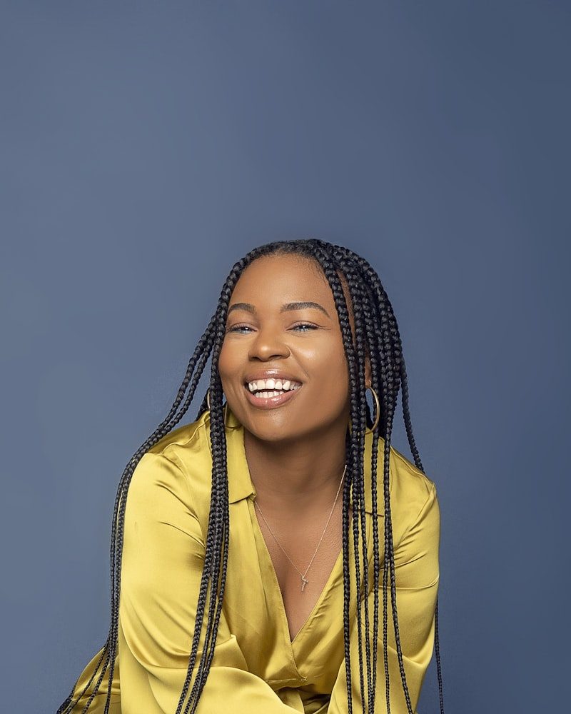 Kundin mit hüftlangen Knotless Braids, lachend vor blauem Hintergrund